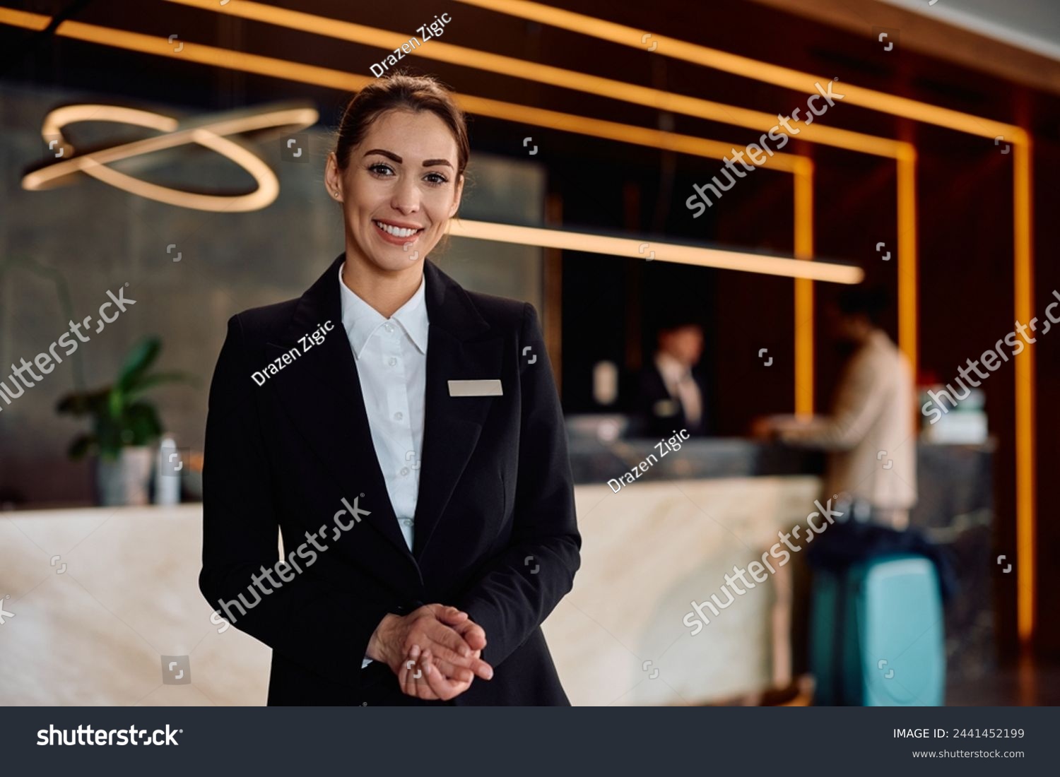 stock-photo-smiling-female-hotel-receptionist-in-a-hallway-looking-at-camera-copy-space-2441452199